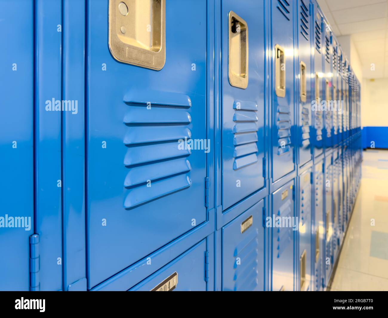 Casilleros de metal azul a lo largo de un pasillo indescriptible en una escuela secundaria típica de EE.UU. No hay información identificable incluida y nadie en el hall. Foto de stock