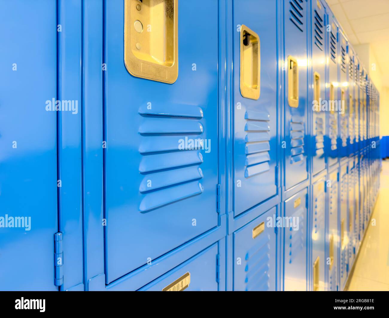 Casilleros de metal azul a lo largo de un pasillo indescriptible en una escuela secundaria típica de EE.UU. No hay información identificable incluida y nadie en el hall. Foto de stock