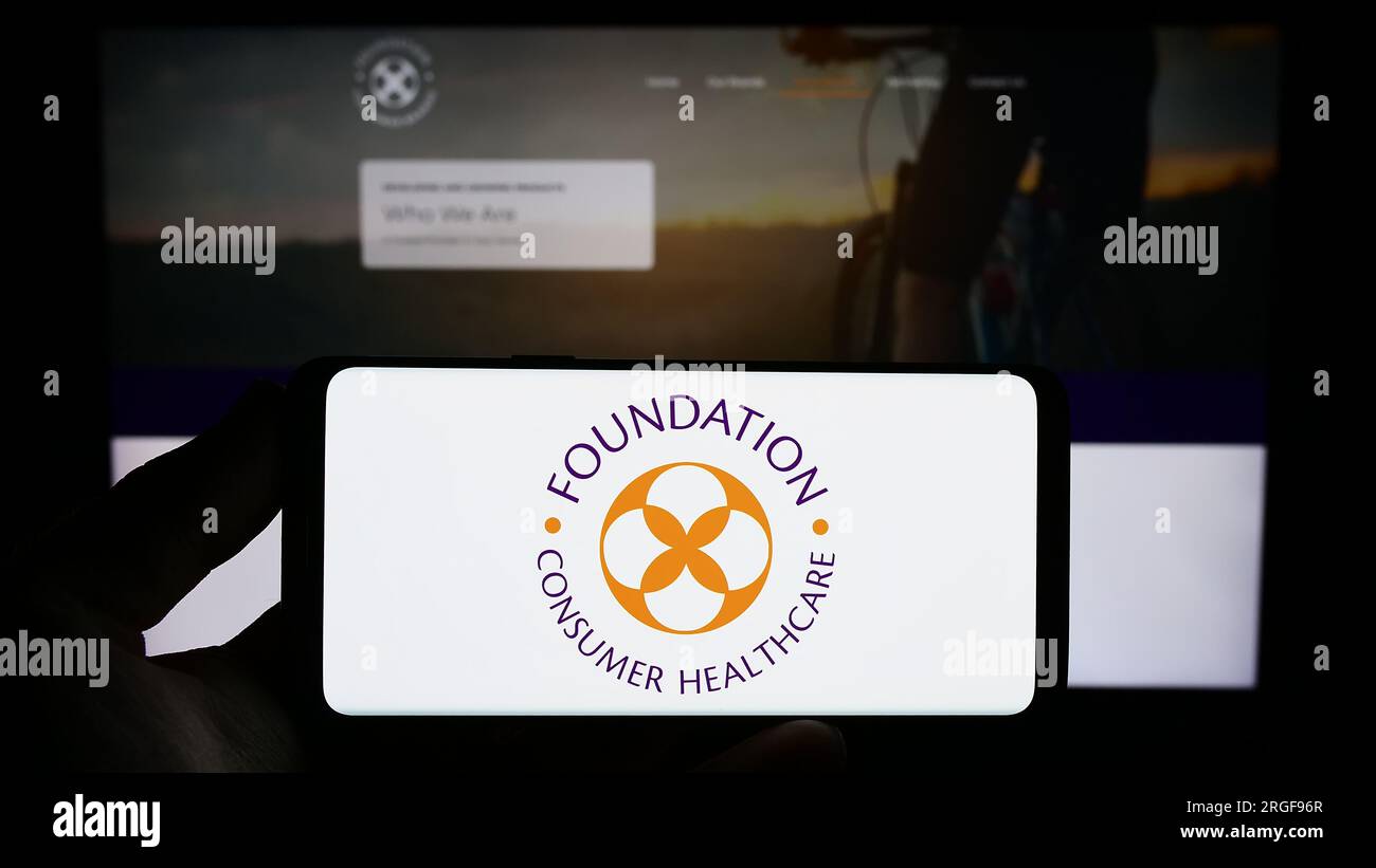 Persona que sostiene el teléfono inteligente con el logotipo de la empresa estadounidense Foundation Consumer Healthcare LLC en la pantalla frente al sitio web. Enfoque en la pantalla del teléfono. Foto de stock