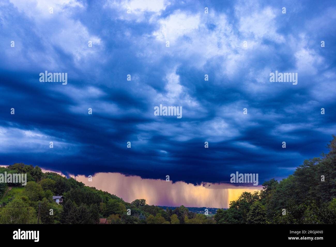 Dramáticas nubes de tormenta con una intensa lluvia iluminada por el sol poniente, Croacia Foto de stock