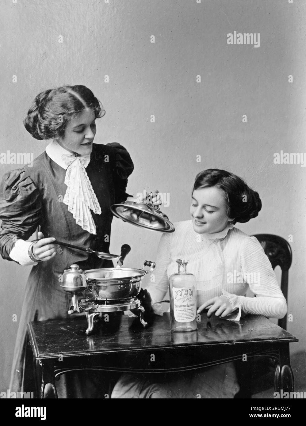 https://c8.alamy.com/compes/2rgmj77/dos-mujeres-usando-utensilios-de-cocina-en-una-demostracion-ca-1912-1930-2rgmj77.jpg