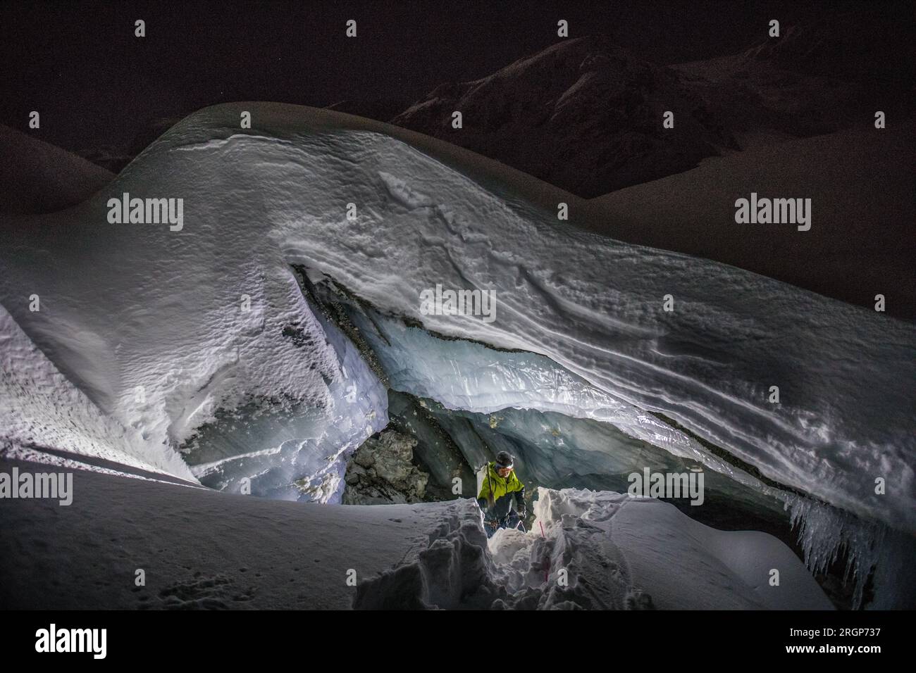 El escalador de hielo emerge de la entrada de la cueva de hielo glacial Foto de stock