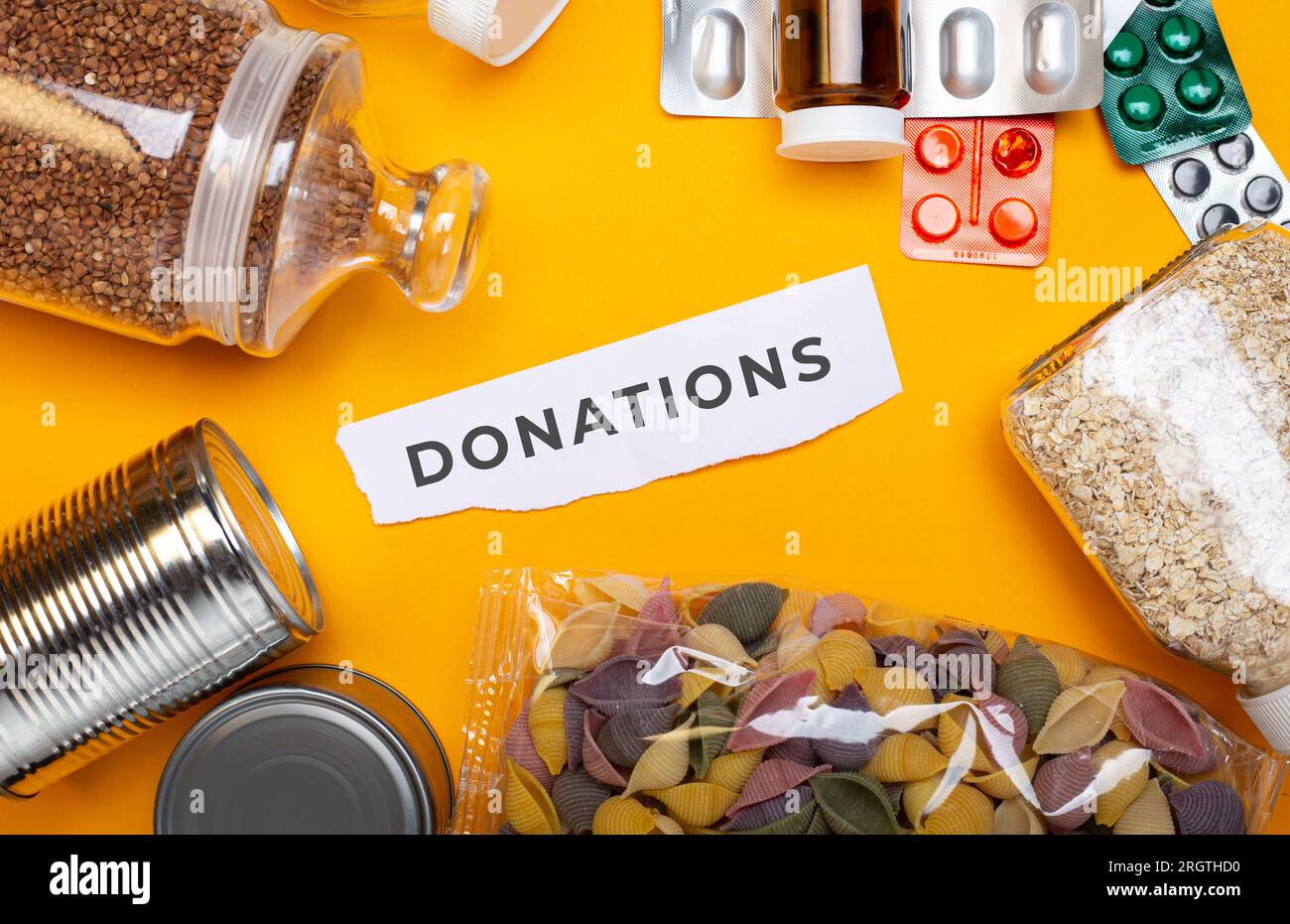 Donaciones de alimentos con comida enlatada sobre fondo de mesa amarillo Foto de stock