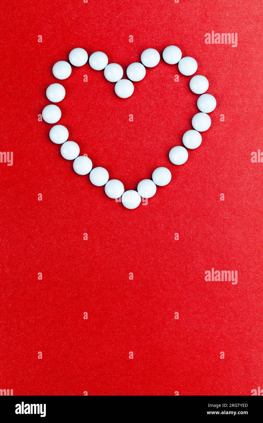 un símbolo del corazón, hecho de medicamentos esenciales, un concepto de tratamiento en cardiología, tabletas de medicamentos médicos apilados en un fondo rojo en forma de Foto de stock