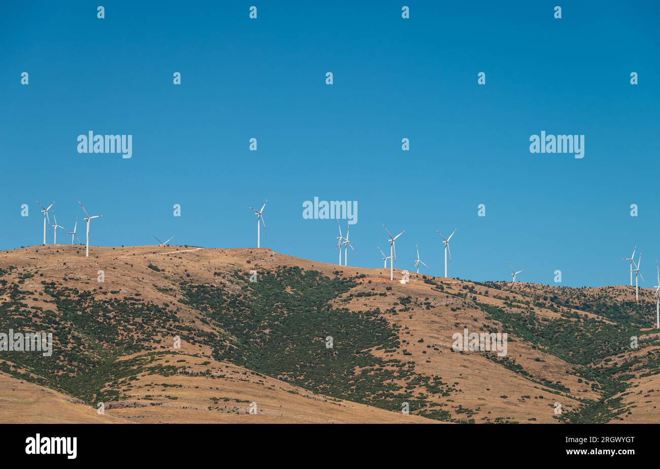 Turbinas eólicas de pie en una colina y generando electricidad en el cielo azul soleado Foto de stock
