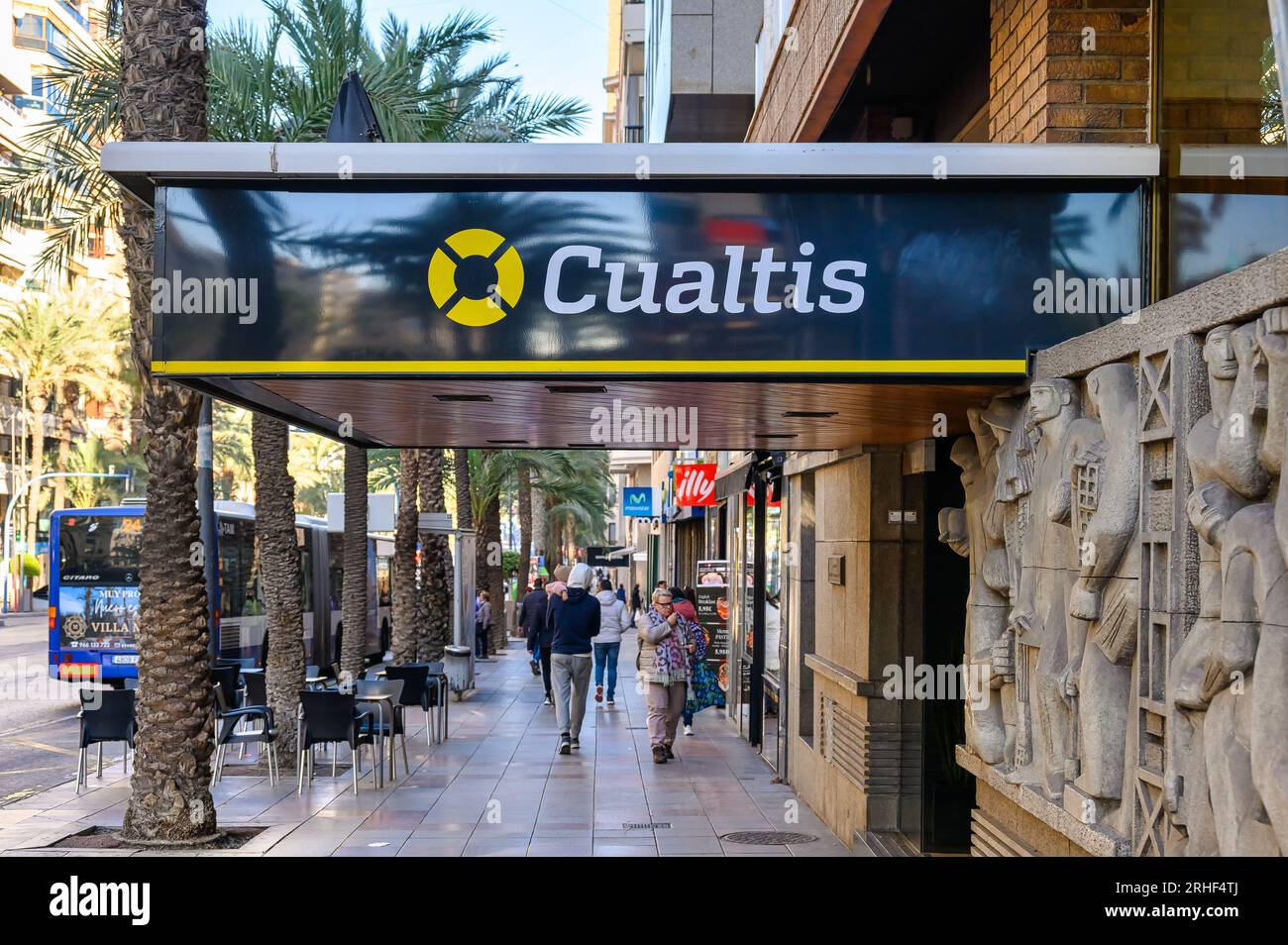 Alicante, España, gente caminando en una acera por el logo de Cualtis business. La empresa ayuda a otros a gestionar los riesgos laborales. Foto de stock