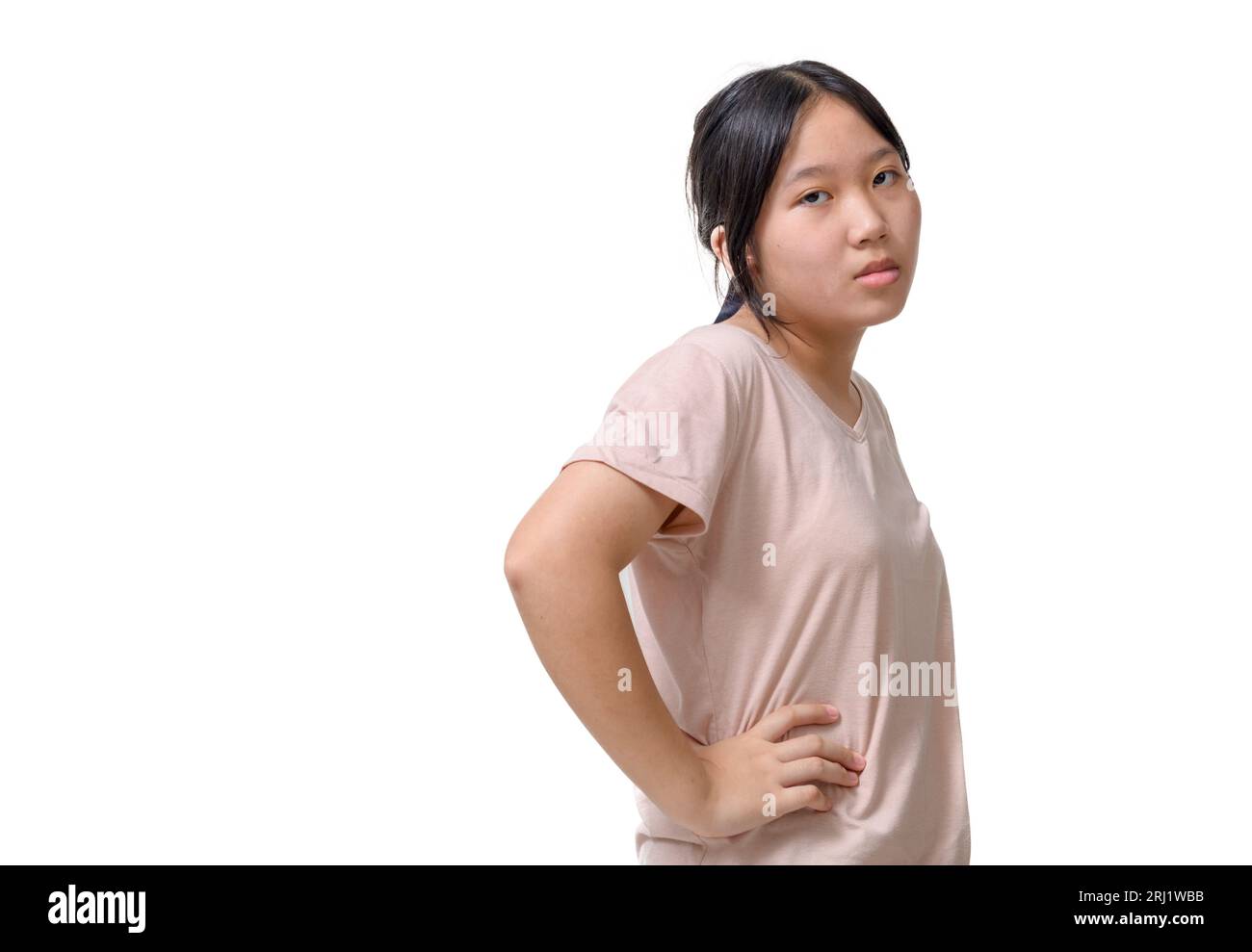 Chica asiática triste y aburrida que se ve reacia y sin diversión en la cámara, cara inclinada en la mano, de pie sobre fondo blanco, concepto de emoción Foto de stock