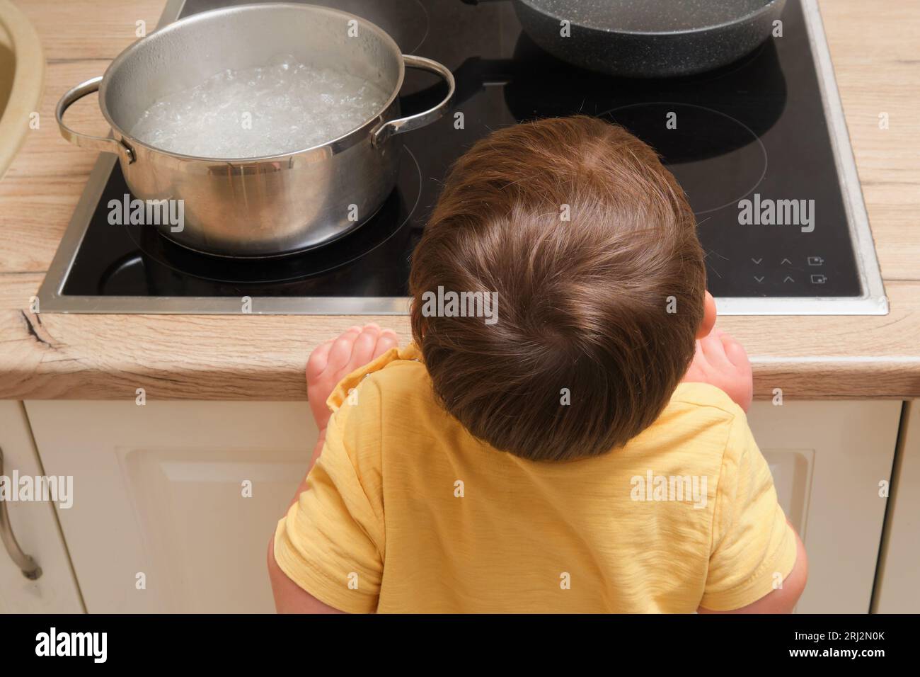 El niño pequeño sostiene un hervidor de agua caliente con agua hirviendo.  Problemas de seguridad de los niños en la habitación de la casa, niño  pequeño Fotografía de stock - Alamy