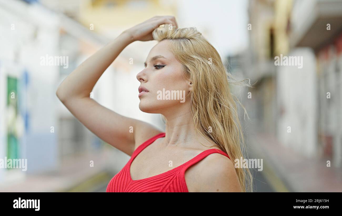 Mujer rubia joven que mira al lado con la expresión seria peinando el pelo  en la calle Fotografía de stock - Alamy