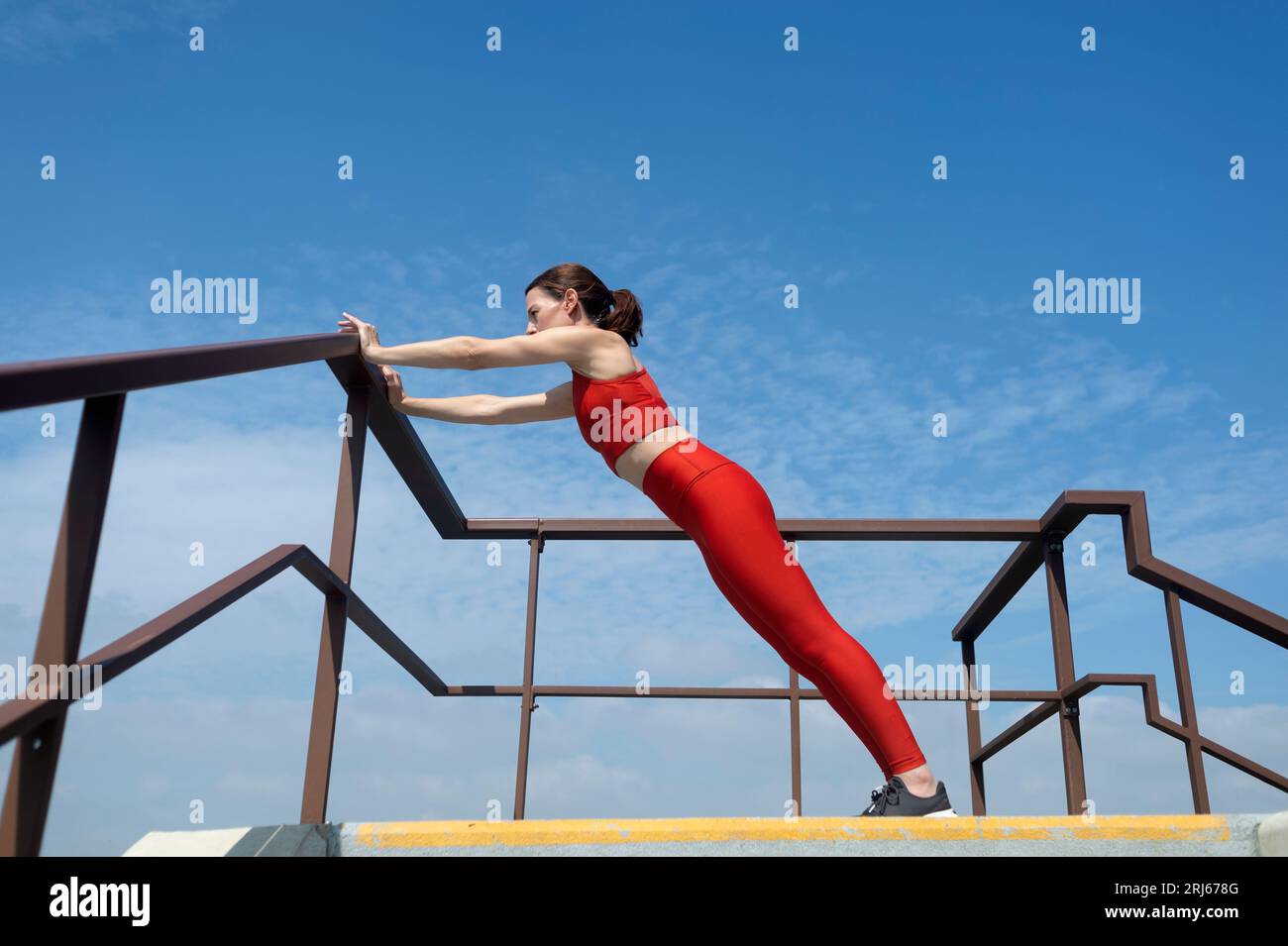 Mujer en forma, deportiva haciendo ejercicios de estiramiento y empuje hacia arriba afuera. Concepto de fitness al aire libre. Foto de stock
