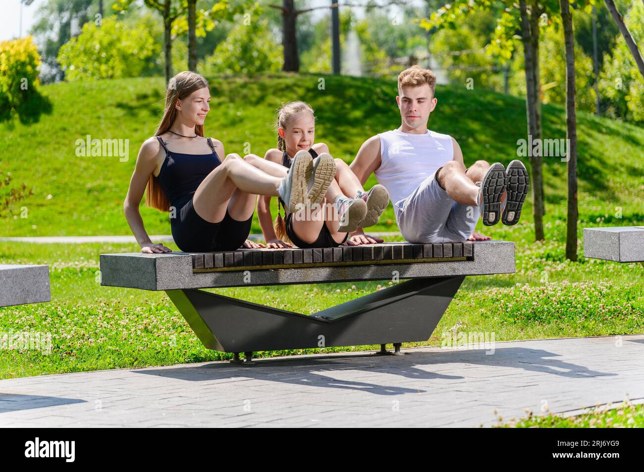 Ejercicio de abdominales de entrenamiento de la familia joven sentado en un banco del parque. Madre padre e hija bomba de prensa en el parque. Foto de stock