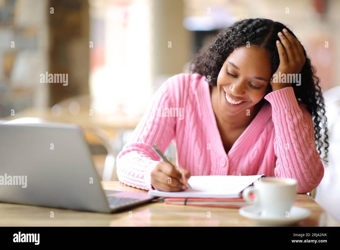 Estudiante negro tomando notas elearning con computadora portátil en una terraza de cafetería Foto de stock
