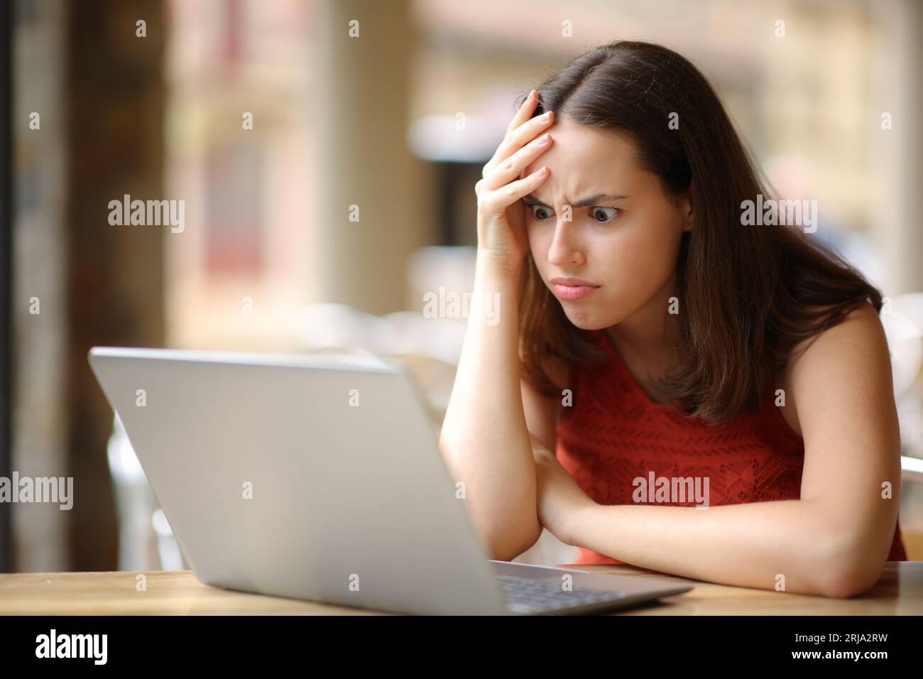 Mujer frustrada masticando portátil después de error en una terraza del bar Foto de stock
