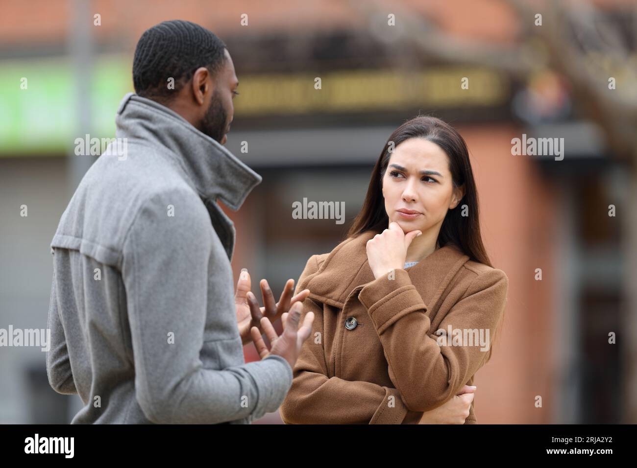 Mujer sospechosa escuchando a un hombre hablando en invierno en la calle Foto de stock