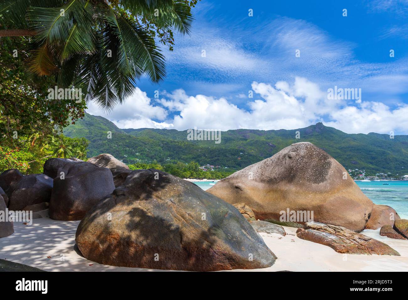 Paisaje de la playa de Beau Vallon, Seychelles. Vista costera con arena blanca y piedras costeras y palmeras bajo el cielo azul en un día soleado de verano Foto de stock