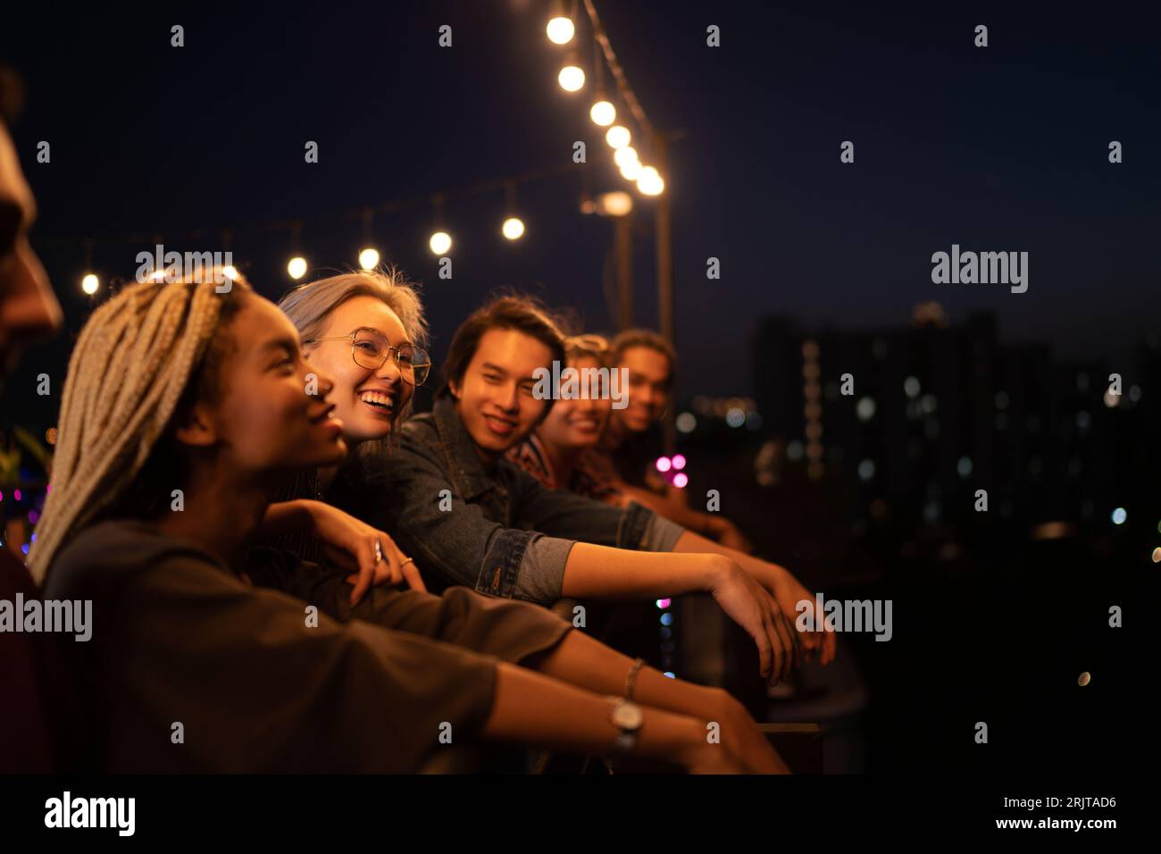 Amigos sonrientes que pasan tiempo libre en la azotea por la noche Foto de stock