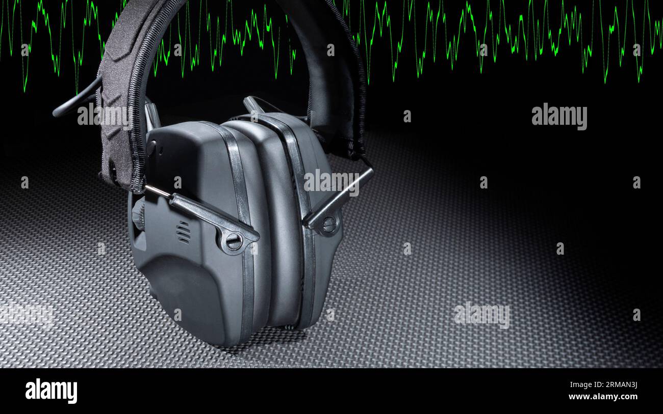 Copia el espacio junto a los auriculares electrónicos para proteger la audición con una onda sinusoidal verde detrás Foto de stock