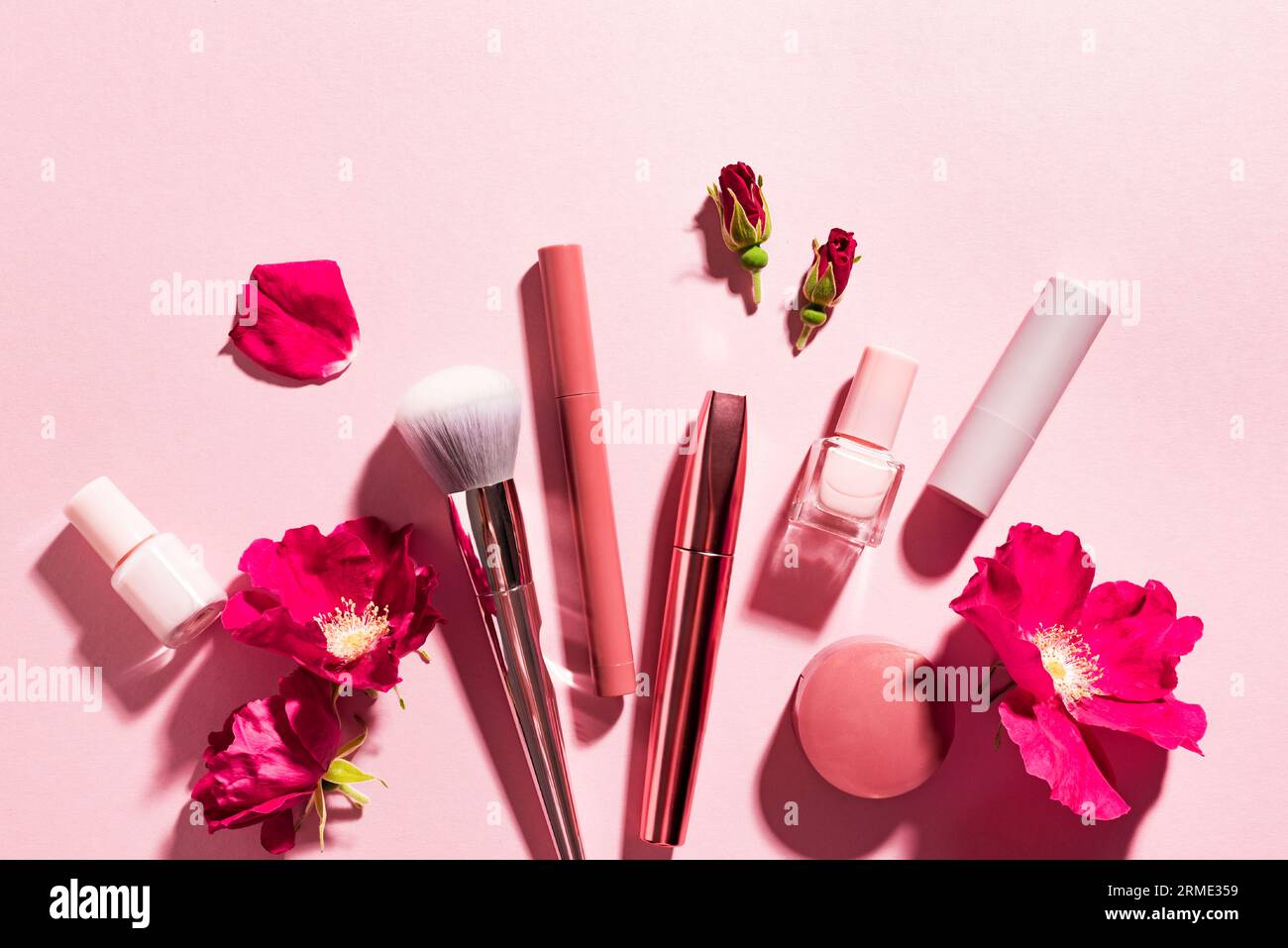Concepto de belleza. Maquillaje productos y flores de rosa sobre fondo rosa pastel, creativo plano lay, espacio de copia. Venta de cosméticos decorativos o cuidado de la piel desi Foto de stock