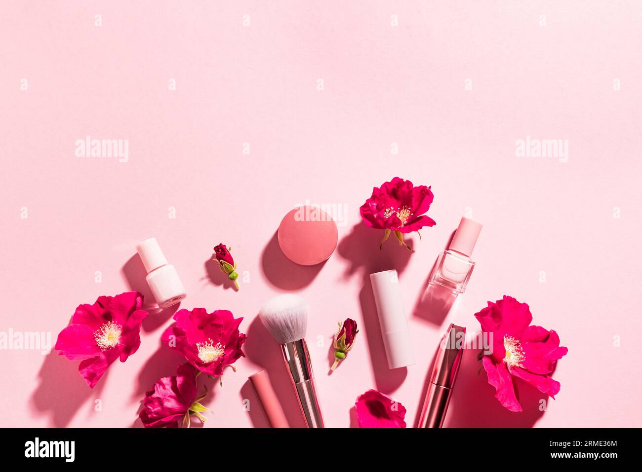 Concepto de belleza. Maquillaje productos y flores de rosa sobre fondo rosa pastel, creativo plano lay, espacio de copia. Venta de cosméticos decorativos o cuidado de la piel desi Foto de stock