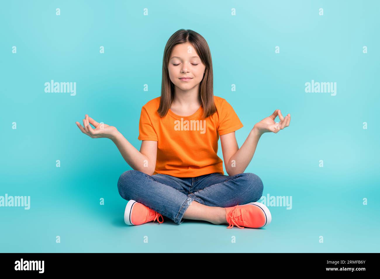 Foto de muchacha enfocada bonita vestida ropa naranja elegante sentada  meditación de yoga en el piso aislado en fondo de color cian Fotografía de  stock - Alamy