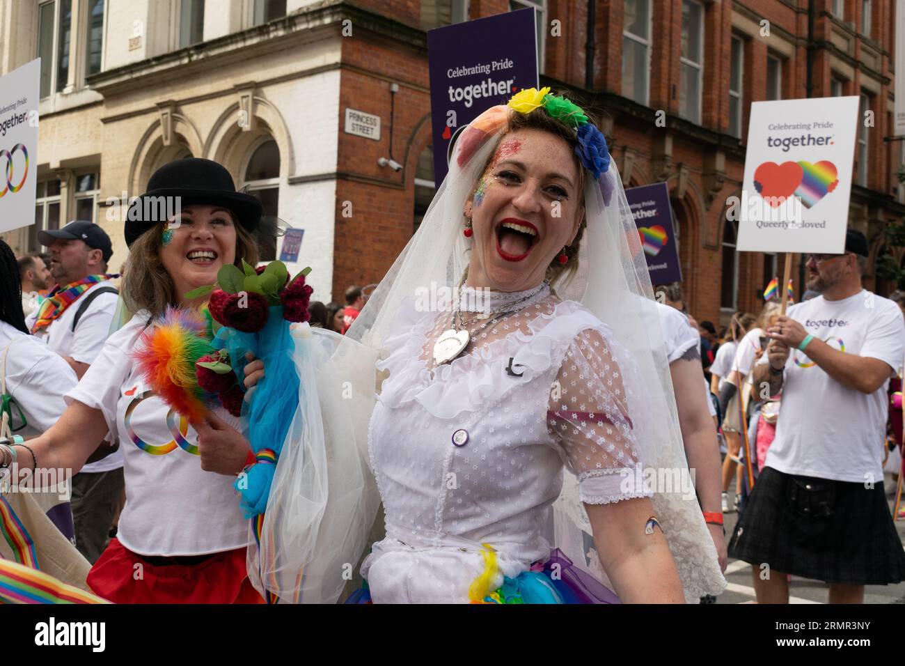 Desfile del Orgullo de Manchester 2023. Dos mujeres en vestidos de novia celebrando aniversario de matrimonio Igualdad.Tema Queerly Amado. Foto de stock