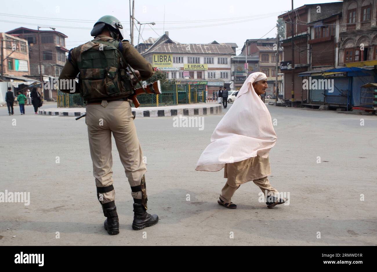 (141023) -- SRINAGAR, 23 de octubre de 2014 -- Un soldado paramilitar indio se pone de guardia mientras una mujer musulmana cachemira pasa por delante durante la huelga contra la visita del primer ministro indio Narendra Modi a Srinagar, capital de verano de Cachemira controlada por la India, el 23 de octubre de 2014. Modi llegó a Srinagar el jueves para celebrar el festival hindú de luces con las personas afectadas por las inundaciones. Los grupos separatistas de Cachemira habían convocado una huelga general y protestas contra la visita de los Modi. (Zjy) CACHEMIRA-SRINAGAR-INDIA-PM-VISITA JavedxDar PUBLICATIONxNOTxINxCHN Srinagar OCT 23 2014 a paramilit indio Foto de stock