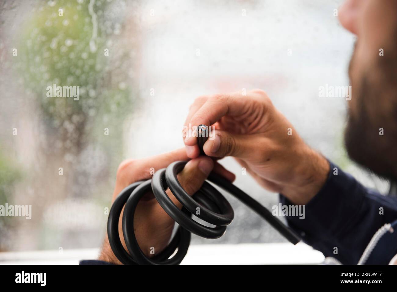 Cierre la mano del electricista sosteniendo el cable eléctrico negro Foto de stock