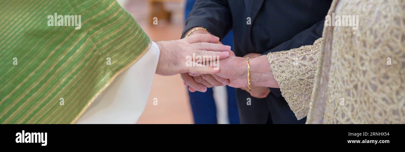 Imagen de las manos de una pareja de ancianos celebrando 50 años de matrimonio mientras el párroco les da la bendición. Banner horizontal Foto de stock