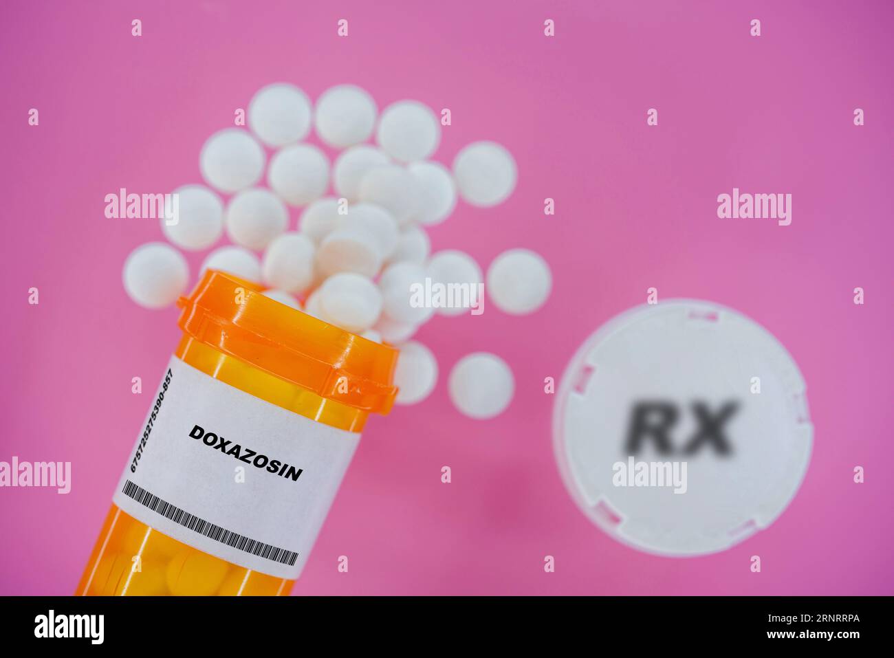 Doxazosin Rx píldoras de medicina en vial pláctico con tabletas. Pastillas derramando desde el contenedor amarillo sobre fondo rosa. Foto de stock