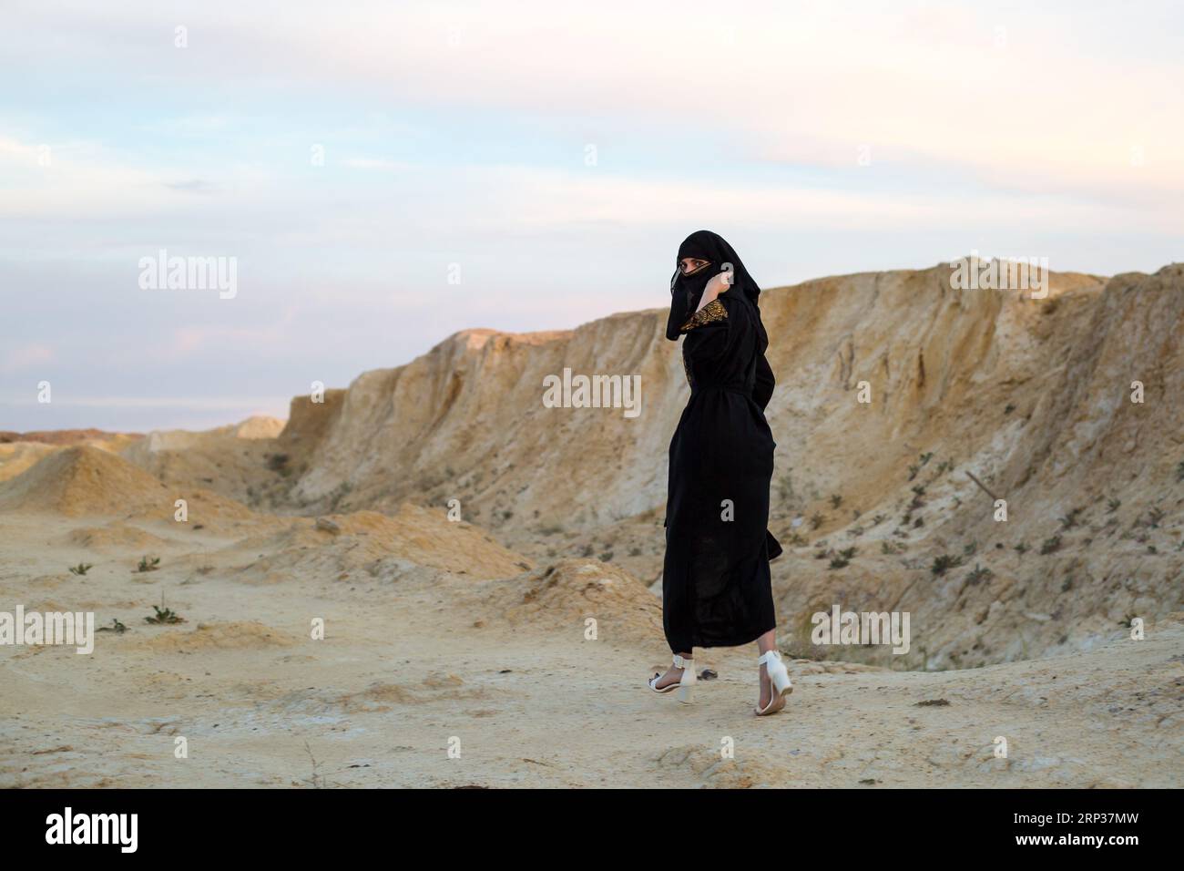 La ropa nacional negra de la mujer del Islam corre a través del desierto del peligro. Foto de stock