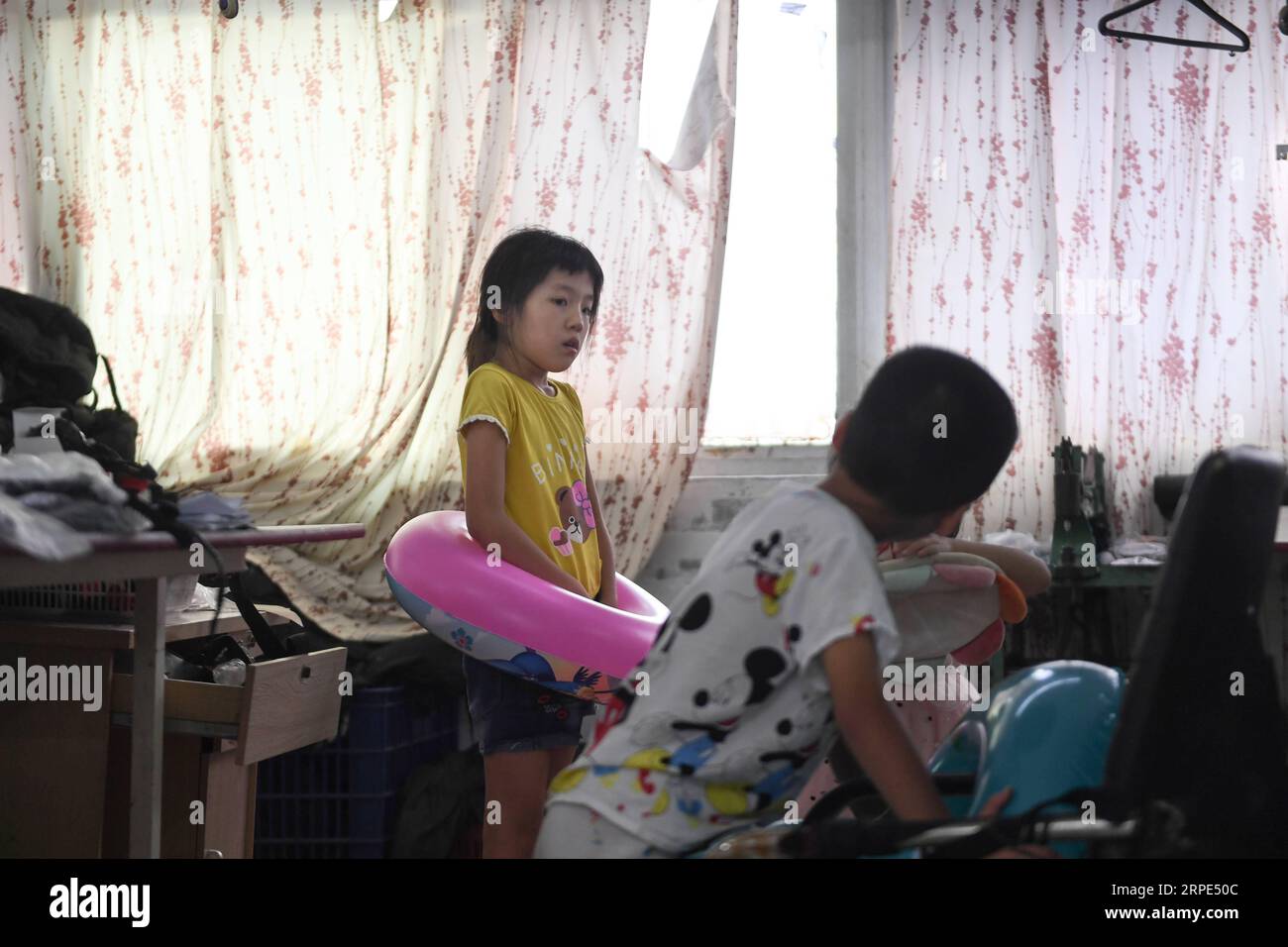 (190818) -- PEKÍN, 18 de agosto de 2019 -- Lu Changli y su hermano Lu Penghan escuchan música en el taller de una fábrica de ropa en Shishi, provincia de Fujian, al sureste de China, el 1 de agosto de 2019. El calor abrasador ha estado envolviendo a Shishi de Fujian, en el sureste de China, este verano, dejando a pocos caminando por las calles normalmente bulliciosas. Por el contrario, las fábricas de ropa, que están densamente diseminadas en la ciudad, están llenas de personas que han sido inundadas con su trabajo, ya que el verano es la temporada alta para la confección de prendas de vestir cada año, y también sus hijos. El reputado estatus de Shishi como un importante manufac de ropa Foto de stock