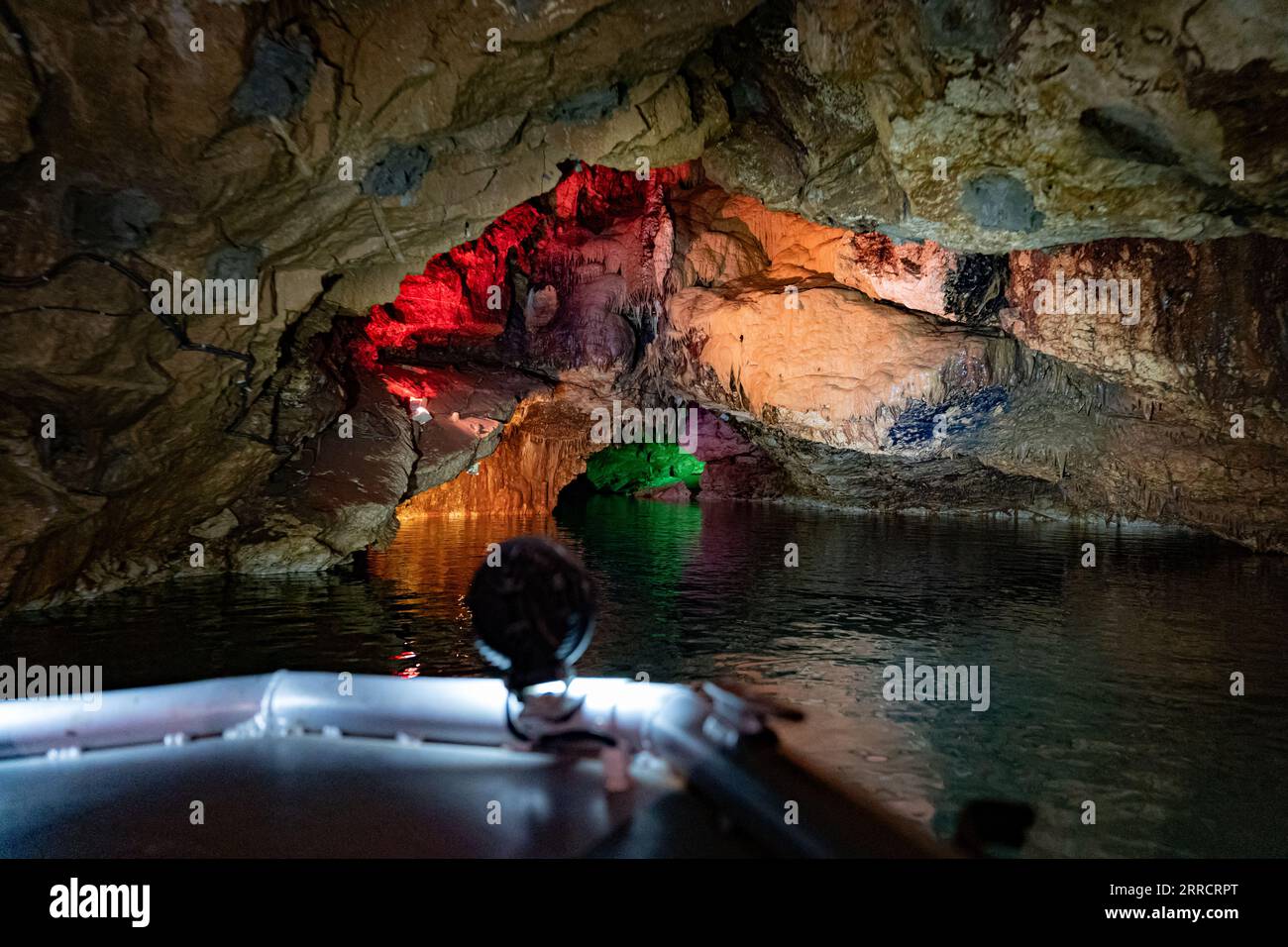 Barco subterráneo del lago de la cueva con paredes iluminadas coloridas Foto de stock