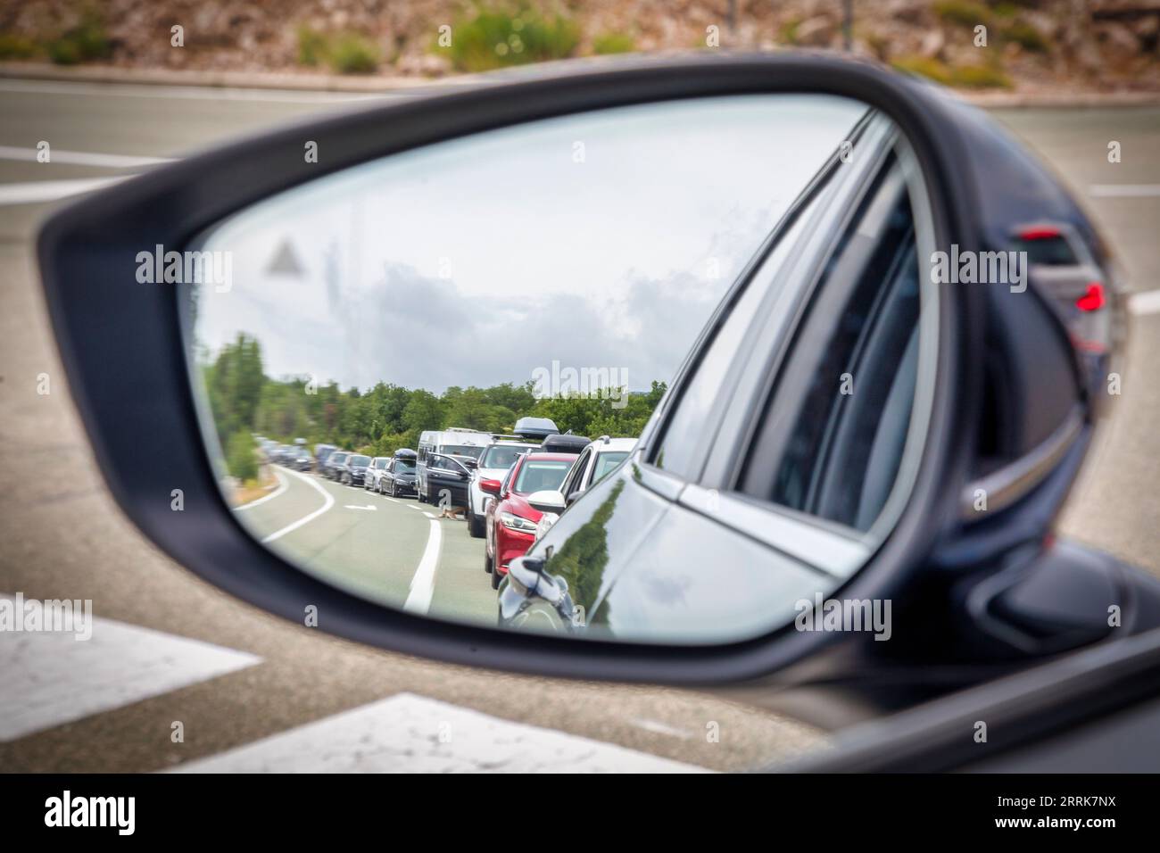 Croacia, Condado de Lika-Senj, municipio de Senj, puerto de Stinica, coches en cola esperando el ferry visto desde el espejo retrovisor exterior del coche Foto de stock
