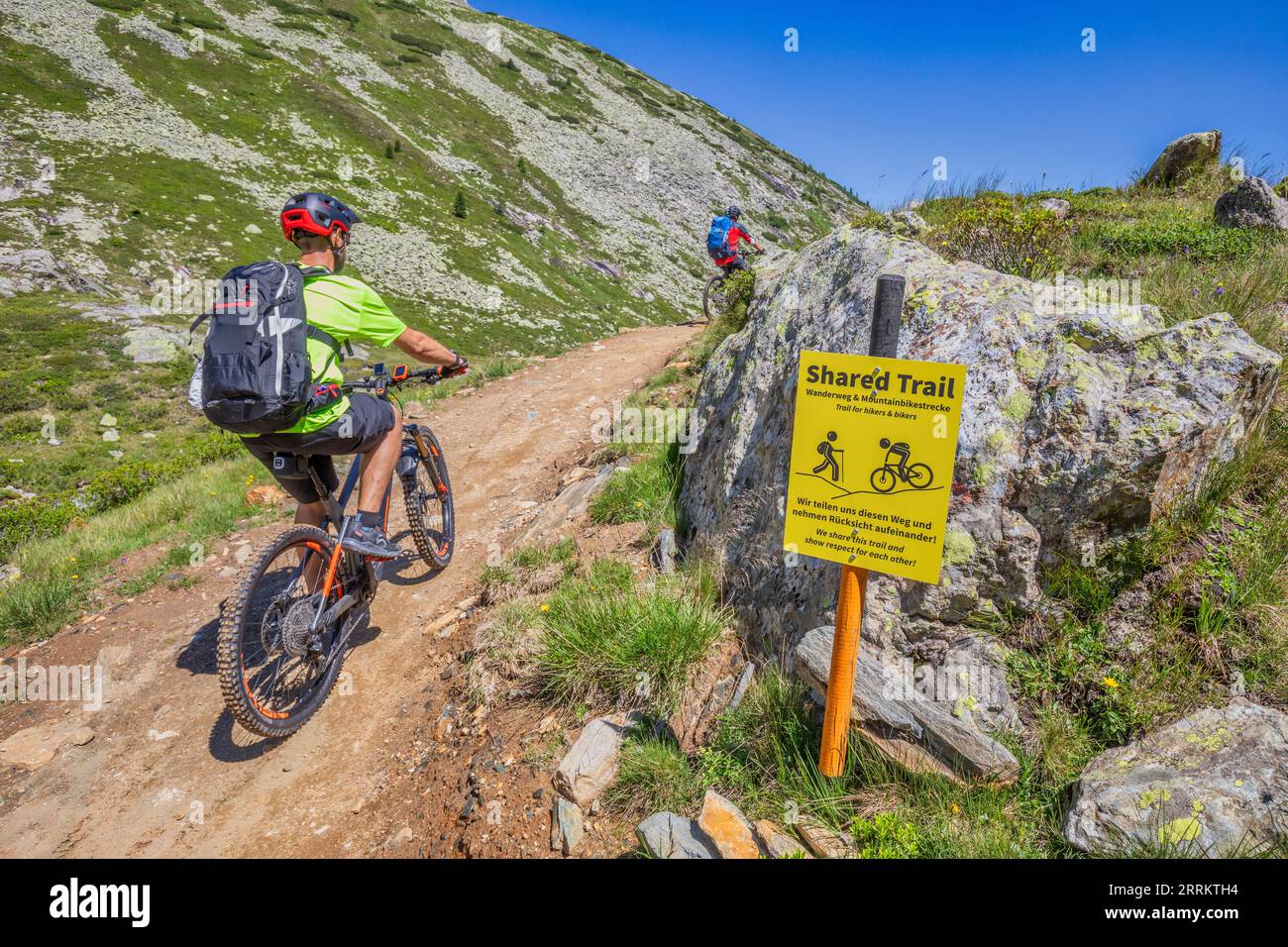 Austria, Tirol, Zillertal, Finkenberg, dos hombres montan sus bicicletas a lo largo del camino compartido entre ciclistas y excursionistas que conduce hasta el Pfitschergründl o Zamsergrund, la mesa nos recuerda la tolerancia mutua Foto de stock
