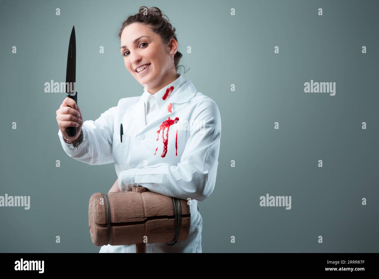 Sosteniendo mazo de madera y cuchillos, una mujer aparentemente benigna de blanco se vuelve inquietante. Simbolizando individuos poco éticos haciéndose pasar por científicos, el im Foto de stock
