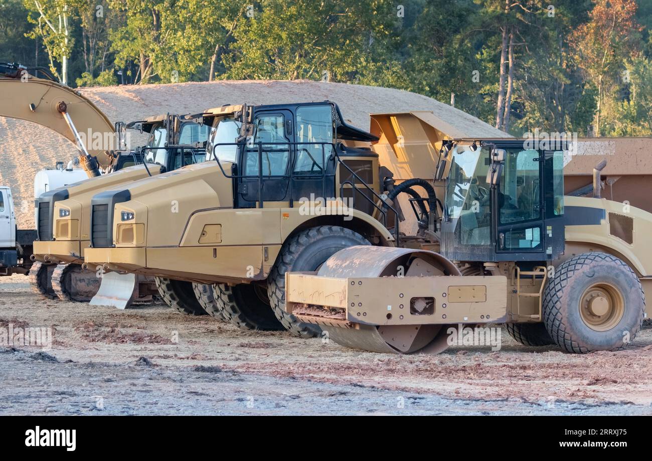 Camiones y equipos pesados en un sitio de construcción cerca de un barrio residencial. Foto de stock