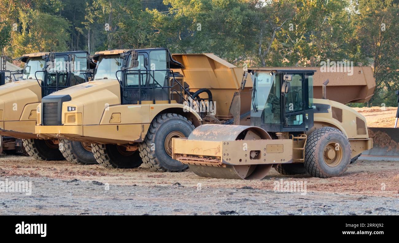 Camiones y equipos pesados en un sitio de construcción cerca de un barrio residencial. Foto de stock