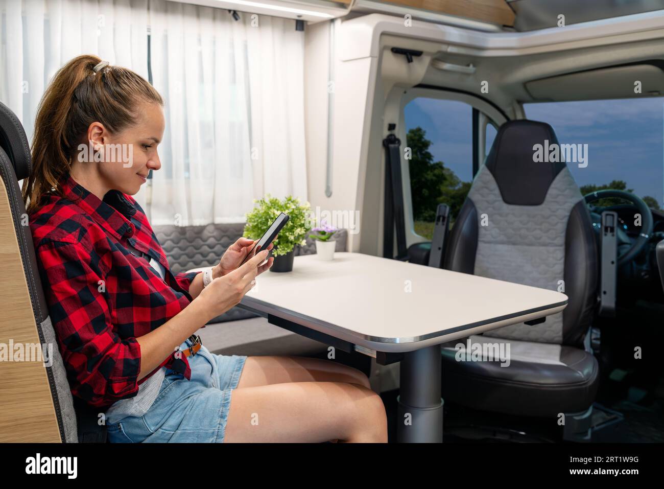 Mujer sentada dentro de la furgoneta y usando su teléfono móvil, viajando en casa rodante. Alquiler de RV. Foto de stock
