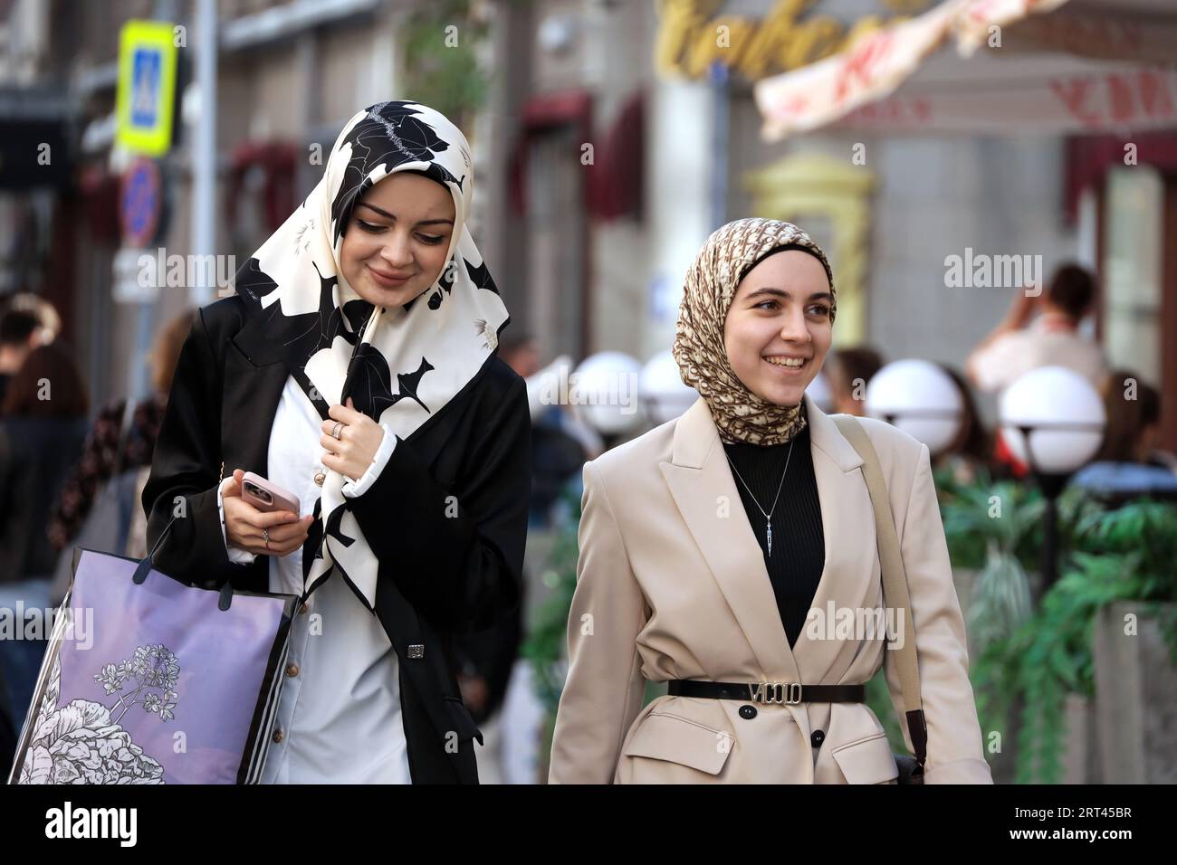 Dos mujeres jóvenes felices en pañuelos caminando en una calle de la ciudad en otoño Foto de stock