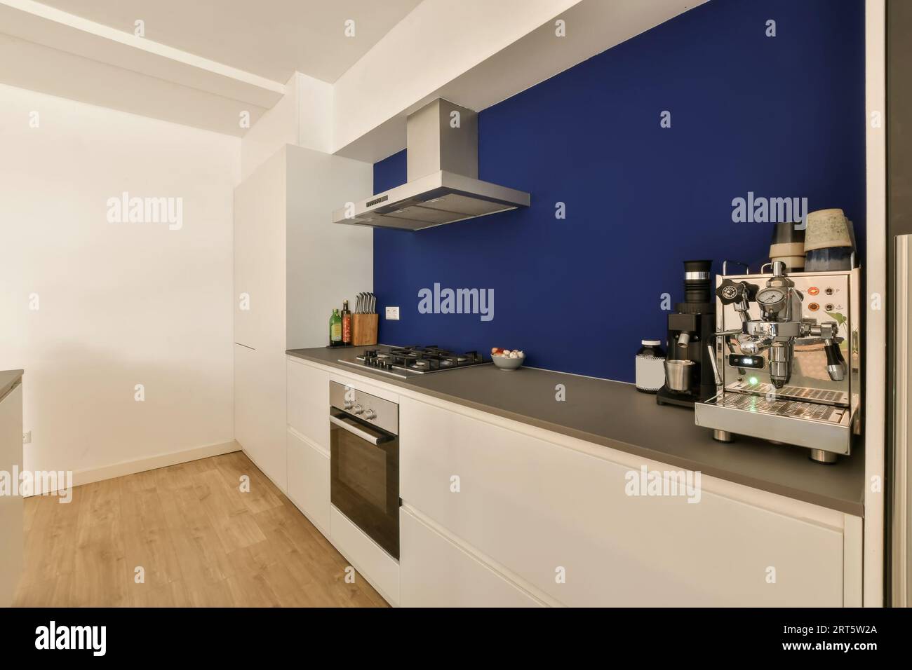 Una cocina con paredes azules y armarios blancos en la pared hay un  televisor de pantalla plana montado encima