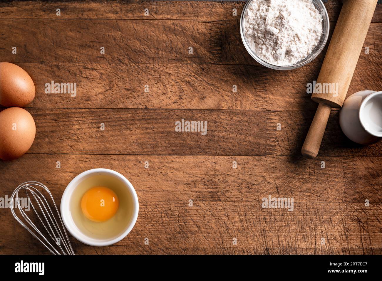 Harina de trigo, huevos, rodillo y batidor sobre fondo de madera, vista superior, espacio de copia. Ingredientes para panadería, panadería o concepto de cocina. Foto de stock