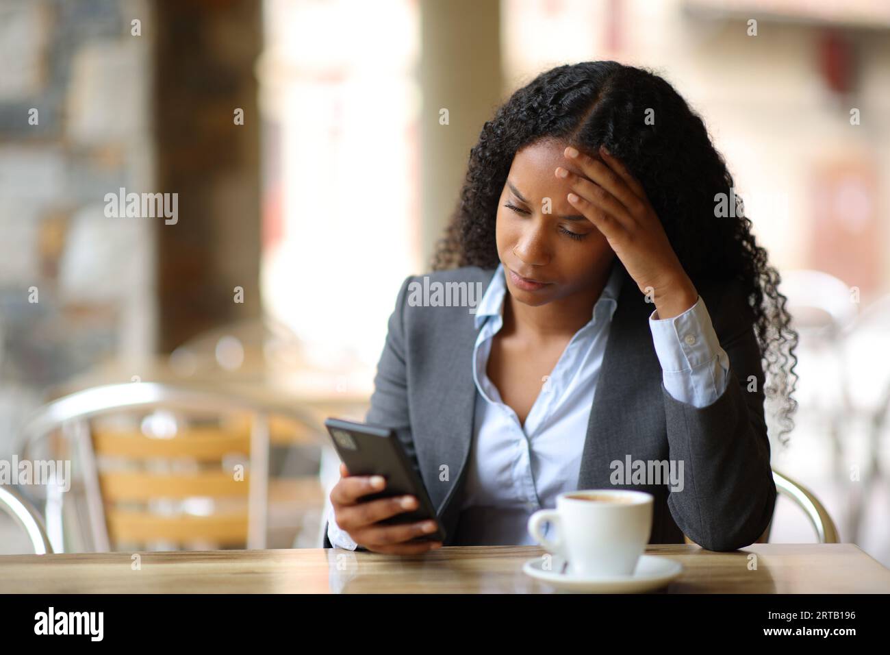 Empresaria negra preocupada que comprueba las malas noticias por teléfono en una terraza del bar Foto de stock