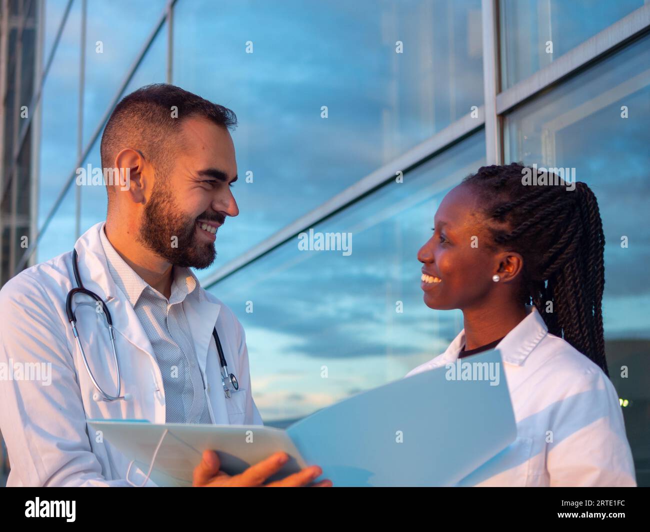 Dos médicos del hospital, una mujer y un hombre, tomando un descanso al aire libre. Mirándose el uno al otro mientras sonríe. Foto de stock