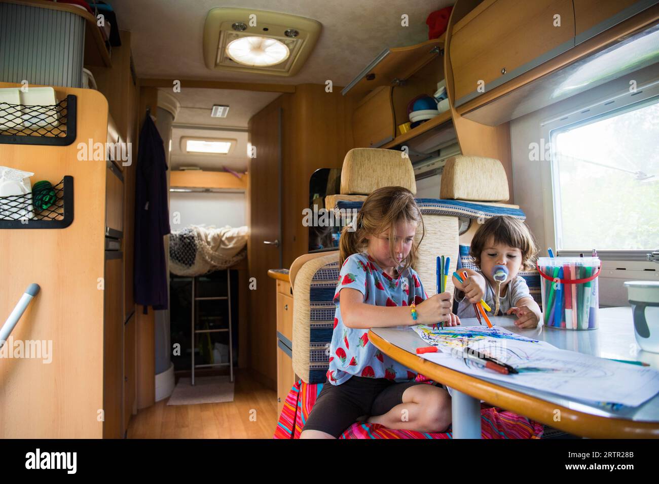 Dos niños caucásicos, hermano y hermana, dibujando dentro de una caravana durante una parada de viaje por carretera. Vacaciones de campista viajando con los niños de fondo con Foto de stock