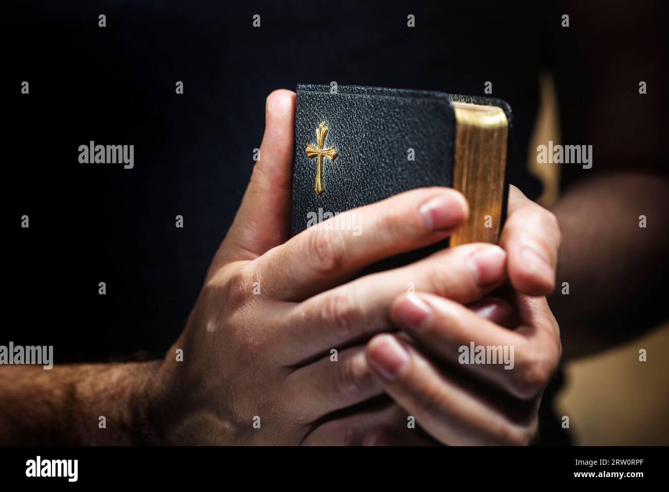 Hombre sosteniendo una vieja pequeña biblia negra en sus manos. Corta profundidad de campo, la nitidez está en la cruz Foto de stock