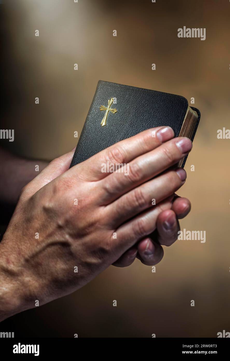 Hombre sosteniendo una vieja pequeña biblia negra en sus manos. Corta profundidad de campo, la nitidez está en la cruz Foto de stock