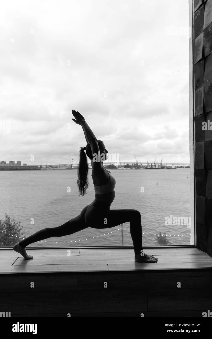 Silueta de mujer joven haciendo yoga en pose de héroe. Concepto de entrenamientos en casa de cuarentena. Espacio publicitario. Foto de alta calidad Foto de stock