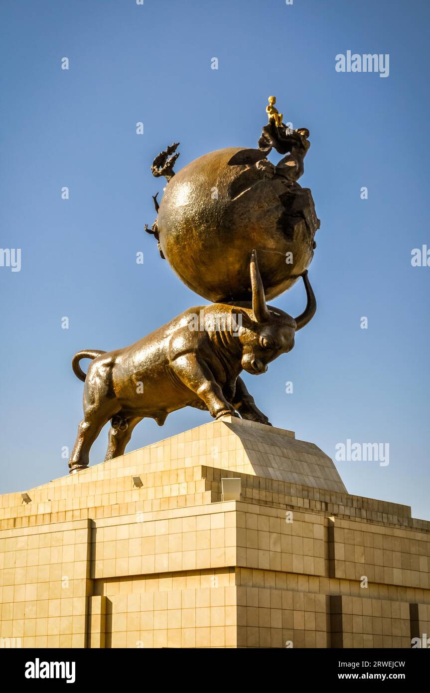 Foto de escultura de toro con bola grande en sus cuernos de pie en la base pedregosa en Ashgabat en Turkmenistán Foto de stock