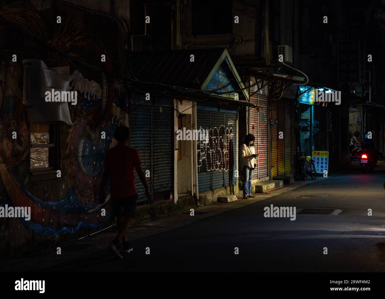 Mujer taiwanesa mirando su teléfono móvil en una calle en la noche, Taipei, Taipei, Taiwán Foto de stock