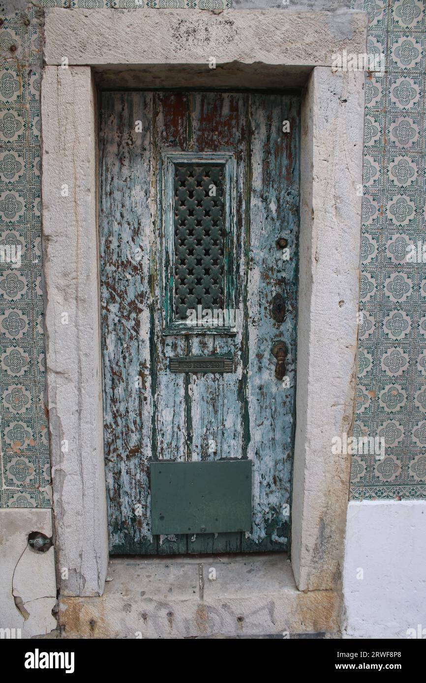 Una puerta de entrada de aspecto vintage con pintura envejecida y parrilla de metal estampado, rodeado de azulejos de pared portugueses con dibujos verdes y blancos. Foto de stock